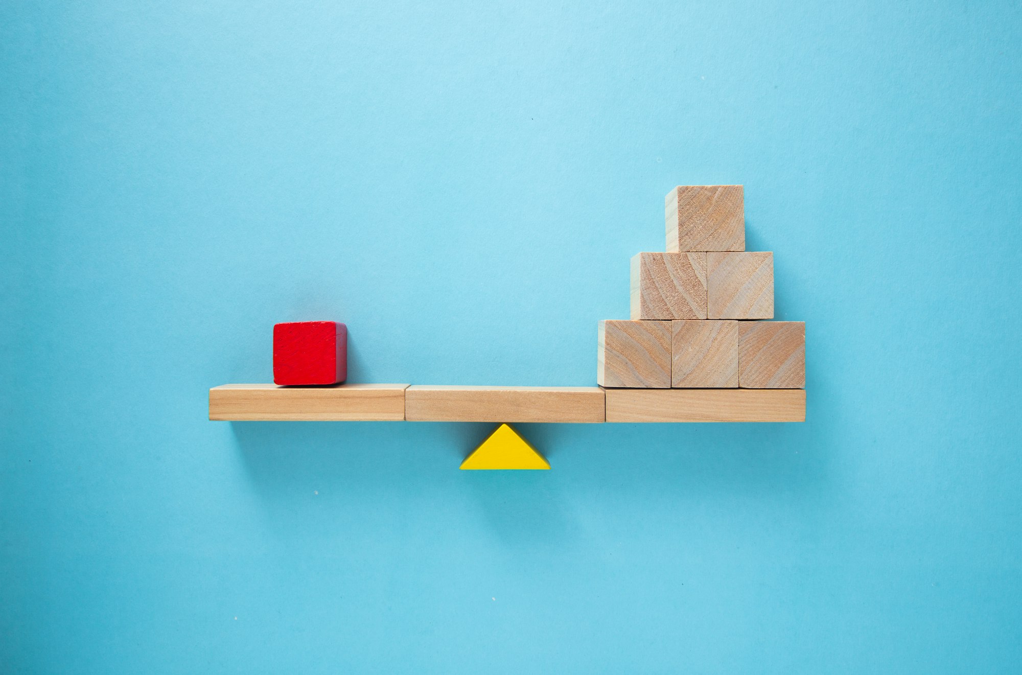 Balancing act: single red block outweighing stack of wooden cubes on seesaw