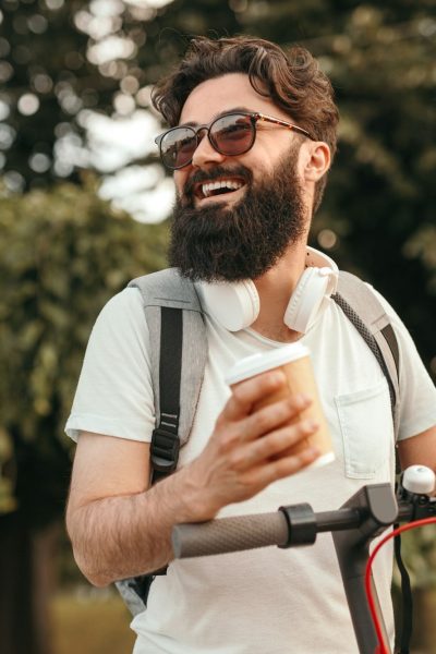 Happy hipster with drink riding scooter